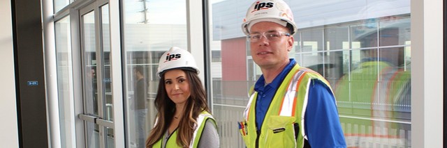 Un homme et une femme, conducteurs de travaux, portant des gilets de sécurité à haute visibilité et des casques de chantier, contre la fenêtre d'un bâtiment.